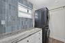 Laundry area featuring white shaker-style cabinetry, stone-patterned countertop, blue vertical subway tile backsplash, and a wall-mounted hanging rod