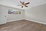Room featuring wood-finish flooring, a multi-blade ceiling fan with integrated lighting, and a large horizontal window