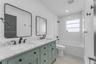 Double vanity with stone-look countertop, green cabinetry with louvered door detailing, matte black fixtures, rectangular wall-mounted mirrors, and a 