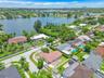 Aerial perspective of a lakefront residential lot featuring a tile roof, paved driveway, masonry wall perimeter, and mature landscaping