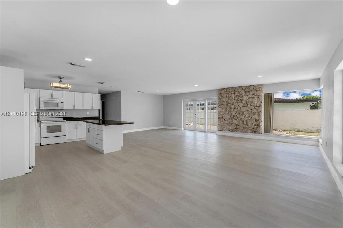 Open-concept interior featuring wood-finish flooring, a kitchen with white cabinetry and dark countertops, a natural stone accent wall, recessed light