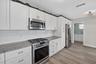 Kitchen featuring white shaker-style cabinetry, stone-patterned countertops, a white subway tile backsplash, stainless steel appliances, and wood-fini