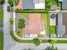 Aerial perspective of a corner lot property featuring a shingle roof, expansive green space, paved driveway, and perimeter fencing