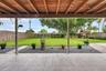Covered patio featuring an exposed wood-beam ceiling, tile flooring, and a fenced backyard with a lawn, crushed stone border, and mature trees