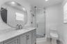 Bathroom featuring a gray vanity with a neutral stone countertop, an oversized circular mirror, a glass-enclosed shower with subway tile surround, and