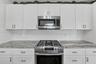 White shaker-style cabinetry with metallic hardware, stone-finish countertops, subway tile backsplash, and stainless steel gas range and built-in micr