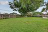 Expansive backyard featuring a large grass lawn, mature shade tree, perimeter wood fencing, and a stone-paver patio area