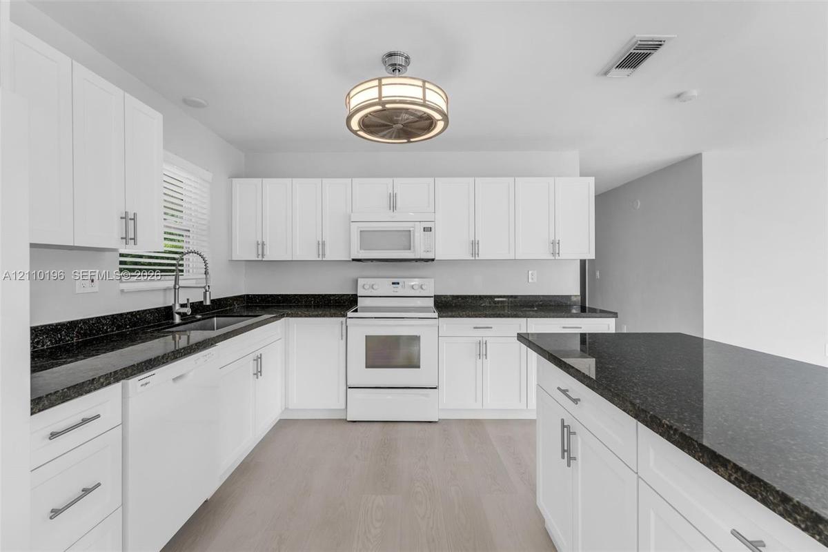 Kitchen featuring white shaker-style cabinetry, dark stone countertops, an integrated island, wood-finish flooring, and a circular drum-style light fi