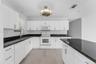 Kitchen featuring white shaker-style cabinetry, dark stone countertops, an integrated island, wood-finish flooring, and a circular drum-style light fi