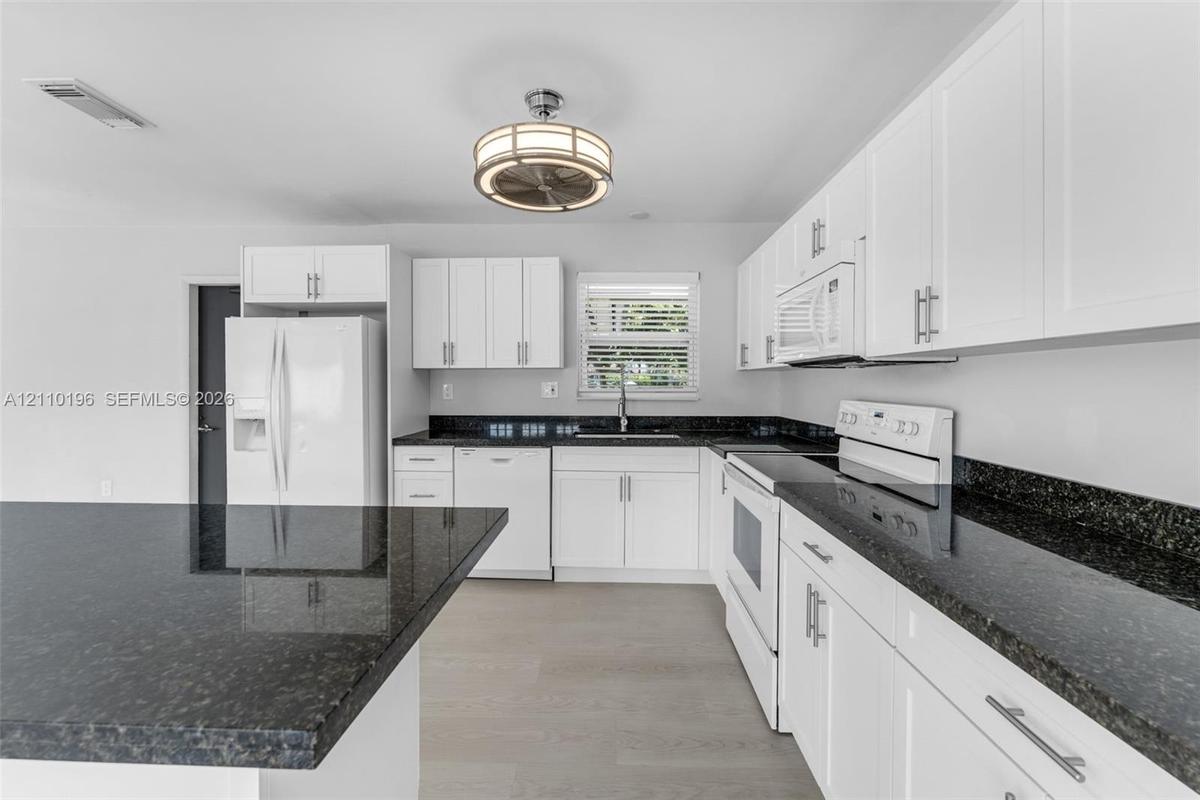 Kitchen featuring white shaker-style cabinetry, dark stone countertops, an integrated island, wood-finish flooring, and a drum-style ceiling light fix