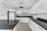 Kitchen featuring white shaker-style cabinetry, dark stone countertops, an integrated island, wood-finish flooring, and a drum-style ceiling light fix