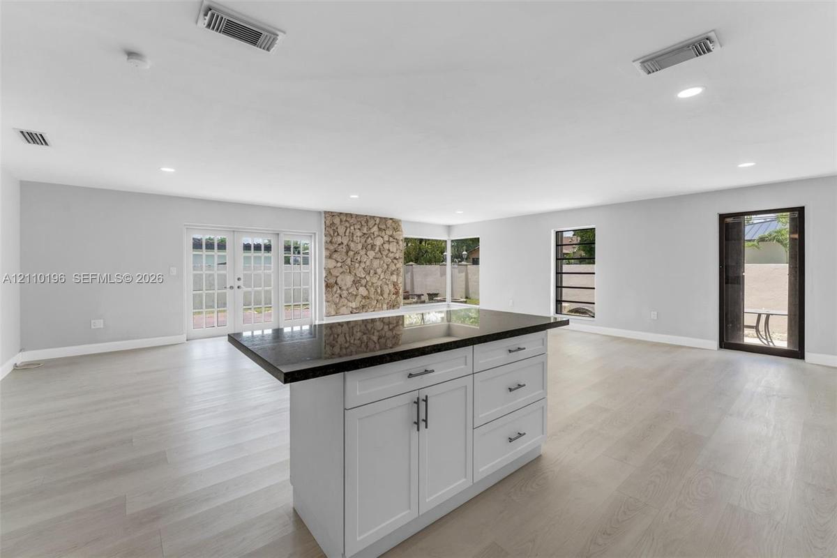 Center island featuring shaker-style cabinetry, dark stone countertop, and recessed lighting, accented by a floor-to-ceiling natural stone feature wal