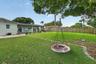 Expansive backyard featuring a covered patio, a manicured lawn, perimeter wood fencing, and mature trees