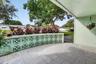Covered patio featuring large-format stone-style tile flooring and a decorative breeze block privacy wall topped with established tropical foliage