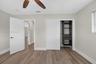 Wood-finish flooring, ceiling fan with wood-tone blades, built-in closet organization system, and white window blinds