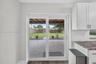 Sliding glass door opening to a concrete patio, covered pergola, fenced backyard with turf, and white shaker-style cabinetry with subway tile backspla