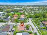 Aerial perspective of a corner lot property featuring a low-slope roof, hardscaped driveway, perimeter block wall, and mature landscaping