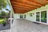 Covered patio featuring a wood-beam ceiling, large-format tile flooring, double glass sliding doors, and a wood privacy fence