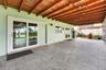Covered patio featuring large-format stone-style tile flooring, exposed wood beam ceiling, dual sliding glass doors, and attached overhead string ligh