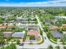 Aerial perspective of a corner lot property featuring a paved driveway, enclosed perimeter wall, mature landscaping, and a multi-section shingle roof