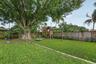 Backyard featuring synthetic turf, concrete paver edging, wood perimeter fencing, and a mature tree