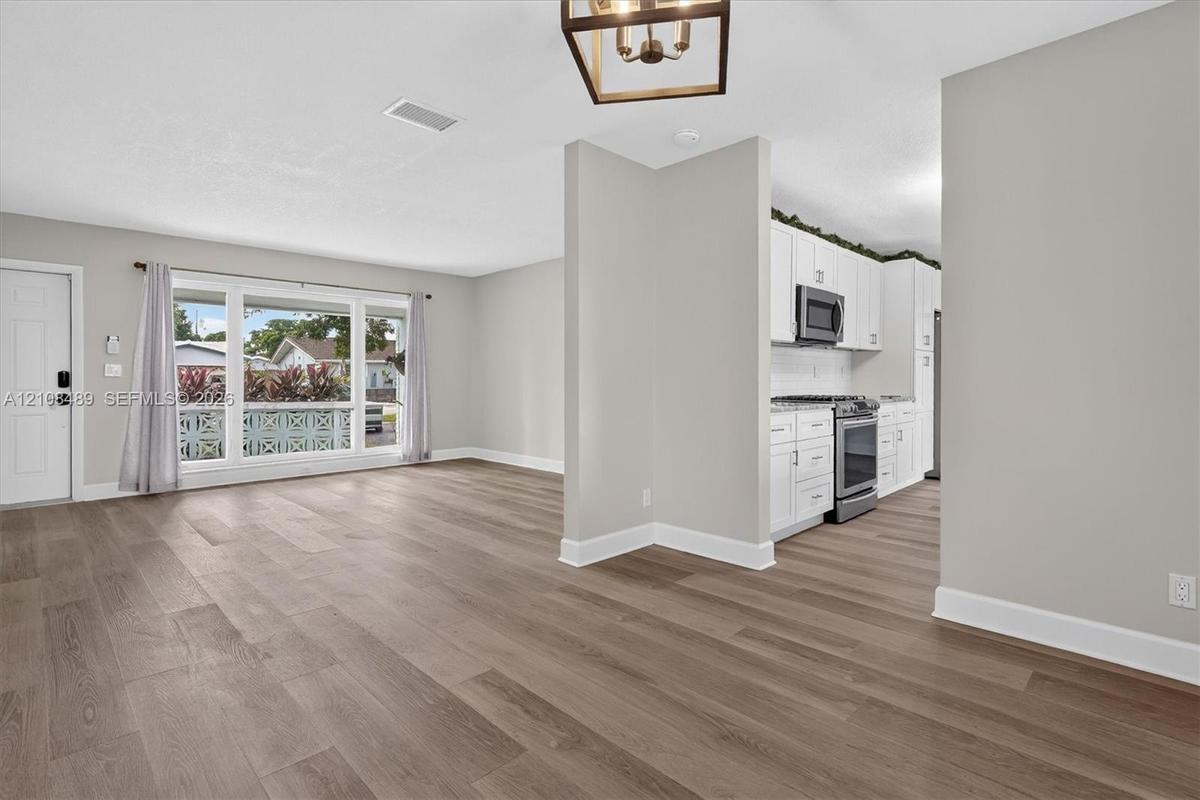 Open interior featuring wood-finish flooring, white cabinetry, integrated stainless steel appliances, a picture window, and a geometric pendant light 