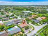Aerial perspective of a single-story residence featuring a hipped roof, paved driveway, masonry perimeter wall, and mature landscaping