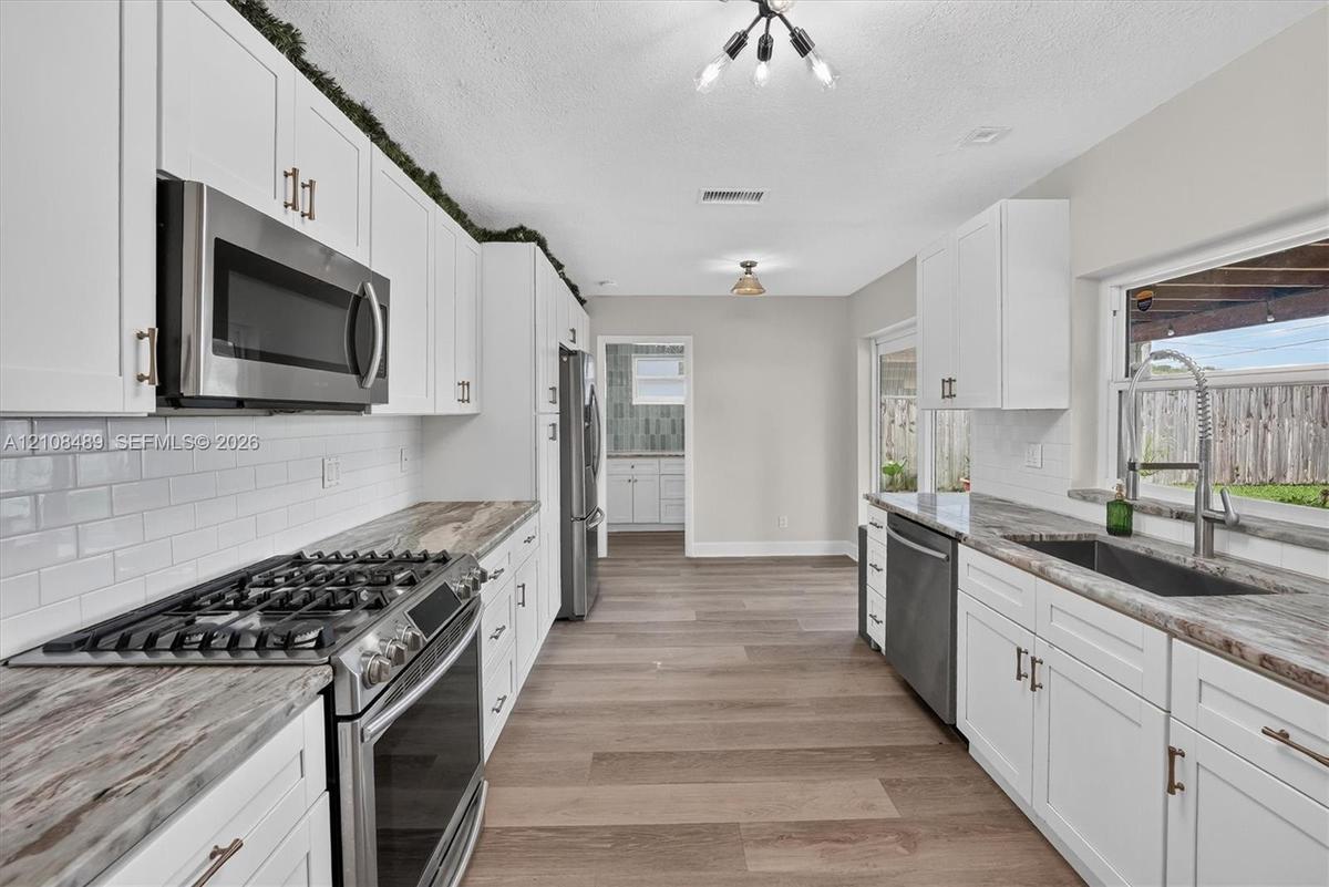 Kitchen featuring white shaker cabinetry, stone-patterned countertops, white subway tile backsplash, stainless steel appliances, and wood-finish floor