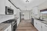 Kitchen featuring white shaker cabinetry, stone-patterned countertops, white subway tile backsplash, stainless steel appliances, and wood-finish floor