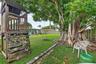 Expansive backyard featuring a mature canopy tree, wood-frame play structure, perimeter wood fencing, and concrete edging