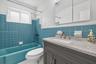 Bathroom featuring a vanity with speckled countertop, integrated sink, and charcoal cabinetry, complemented by teal wall tiling, a matching teal soaki