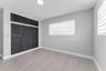 Neutral-toned room featuring wood-finish flooring, built-in floor-to-ceiling louvered-style closet cabinetry with overhead storage, and dual windows w