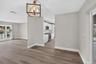 Wood-finish flooring throughout, kitchen featuring white cabinetry and stainless steel appliances, and a geometric metal chandelier