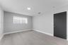 Neutral-toned interior space featuring wood-finish flooring, light gray walls, and a contrasting dark-finished door with metallic hardware