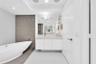 Freestanding soaking tub with a tiled accent wall, single vanity with integrated sink, and large mirror with integrated lighting