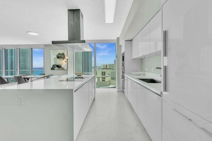 Sleek kitchen featuring an oversized island, integrated cooktop, stainless steel range hood, wall ovens, and custom white cabinetry