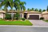 Stucco exterior featuring a multi-hipped tile roof, paver driveway, attached two-car garage, and mature palm trees