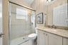 Bathroom featuring a shower with a sliding glass door, tiled wall surround, and a stone-surface vanity with an integrated basin