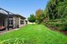 Expansive backyard featuring a screened-in patio, manicured lawn, tiered landscape beds, and mature trees