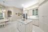 Kitchen featuring custom cabinetry with glass-front display uppers, a central island with stone countertop, stainless steel refrigerator, and tiled fl
