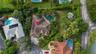 Aerial view featuring a multi-hipped roofline, an in-ground swimming pool, mature palm trees, and landscaped grounds