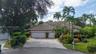 Exterior featuring a tile roof, two-car garage, paver driveway, and mature tropical landscaping