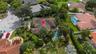 Aerial perspective of a multi-hip roof residence featuring a swimming pool, mature palm trees, dense perimeter landscaping, and a corner lot location