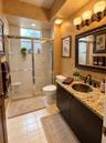 Bathroom featuring a stone-top vanity with a recessed oval basin, framed wall mirror, three-light fixture, and a glass-enclosed shower stall with a ce