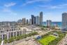 Expansive urban landscape featuring high-rise buildings, distant ocean, and a green space with mature trees