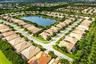 Aerial perspective of a planned community featuring a central lake, paved street networks, tile-roof residential structures, and mature palm trees