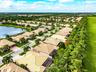 Aerial perspective of residential community featuring tile-roofed homes, waterfront lots, paved roadways, and mature palm tree landscaping