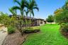 Backyard featuring a screened-in lanai, manicured lawn, established palm trees, decorative rock landscaping, and perimeter shrubbery