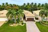 Stucco exterior featuring a multi-hipped tile roof, paver driveway, attached two-car garage, and mature palm tree landscaping
