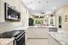 Kitchen featuring shaker-style cabinetry, stone countertops, subway tile backsplash, stainless steel appliances, and three pendant light fixtures